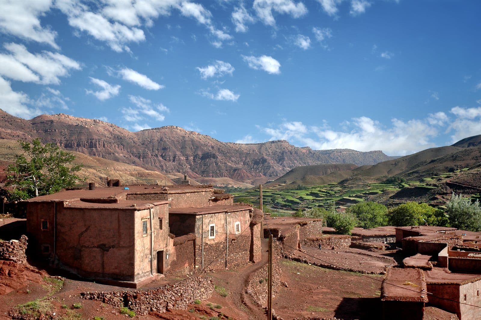 Case di terra a Ouarzazate scaglionate su uno sfondo di montagne sotto un cielo azzurro con nuvole sparse