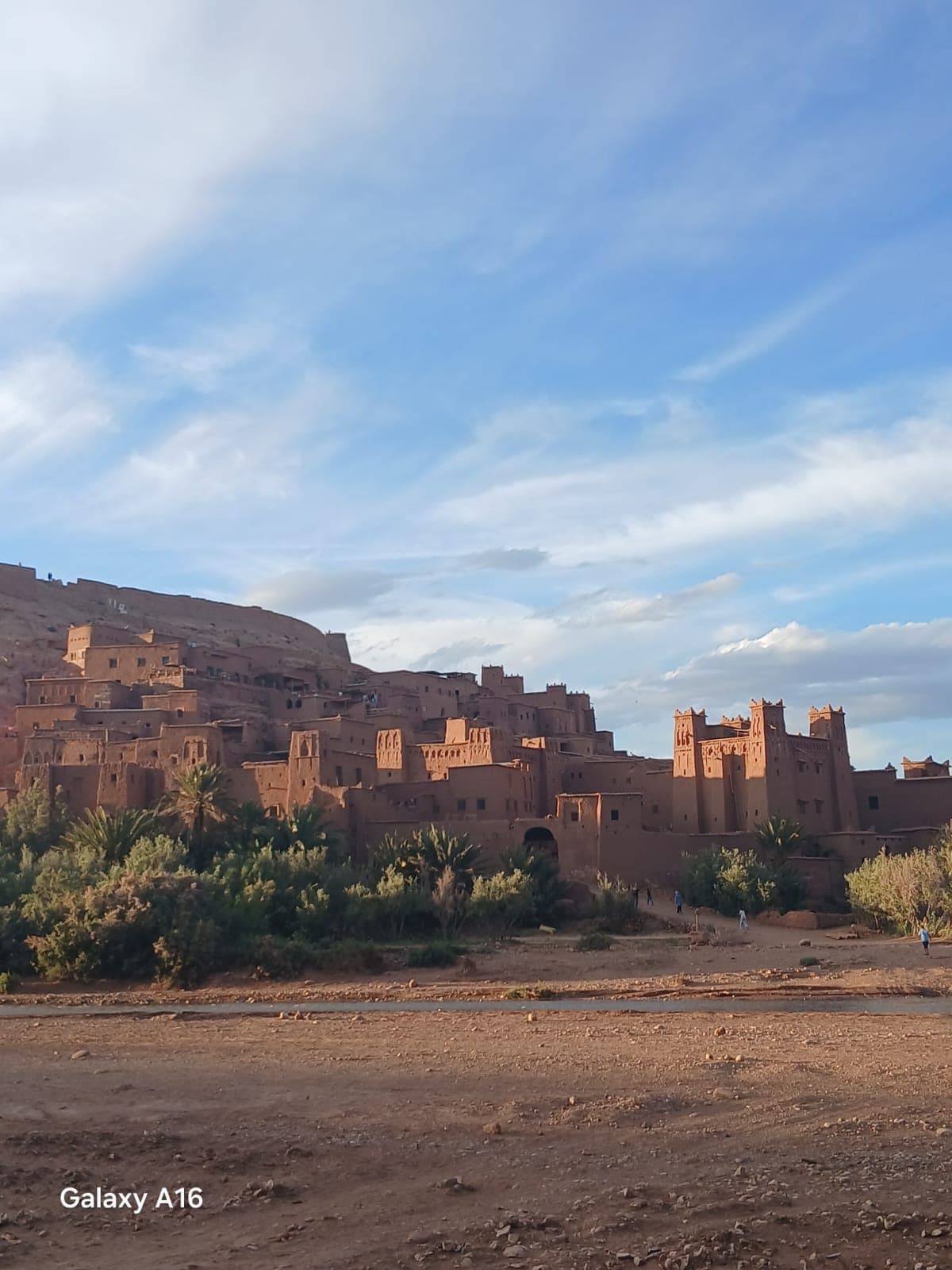The earthen kasbah of Aït Ben Haddou in late afternoon light, tiered mudbrick houses rising above the dry riverbed