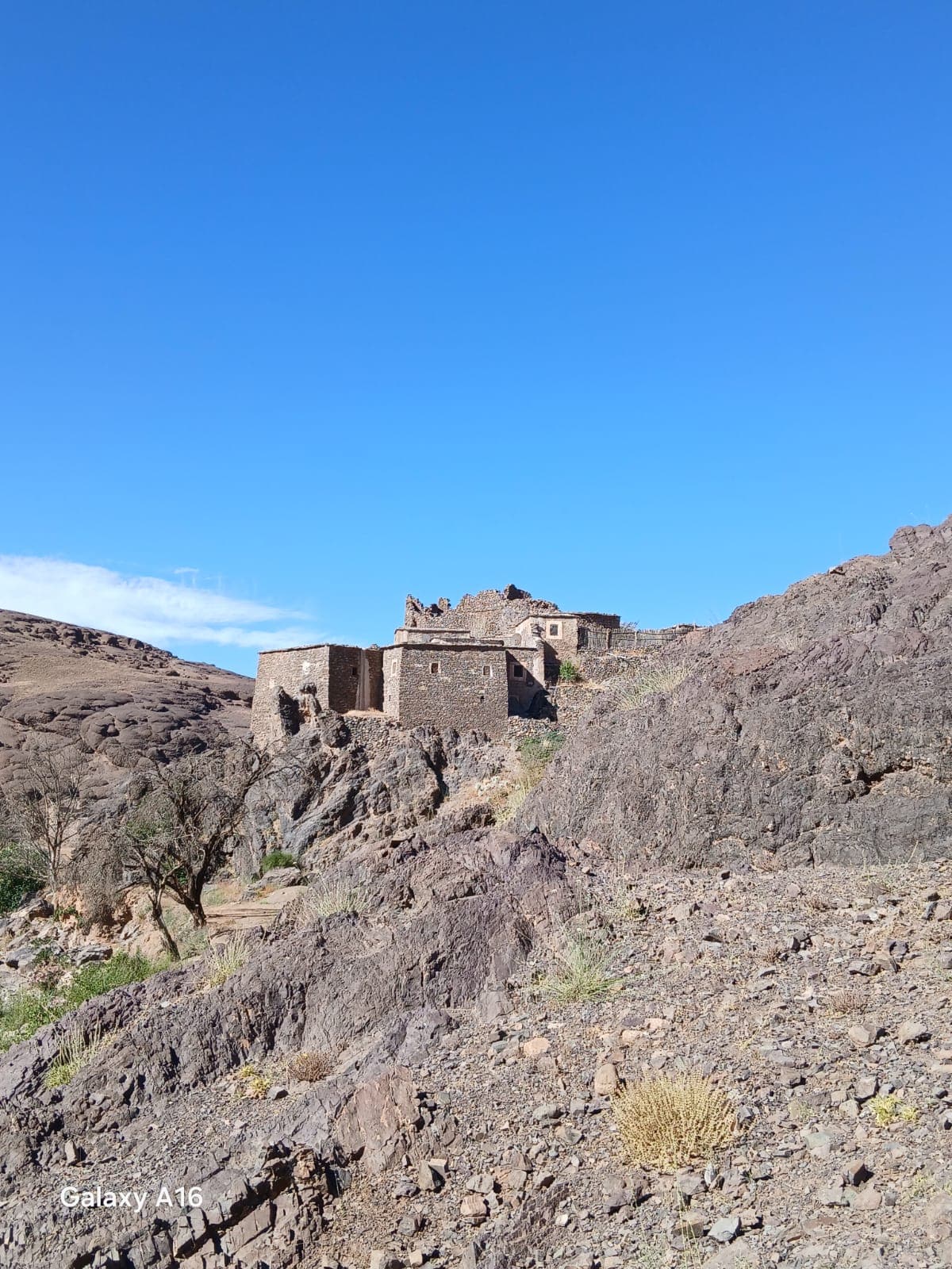 Ein Steindorf auf einem Felssporn im Antiatlas, seine Flachdachhäuser folgen dem Grat über kahlem Hang unter blauem Himmel