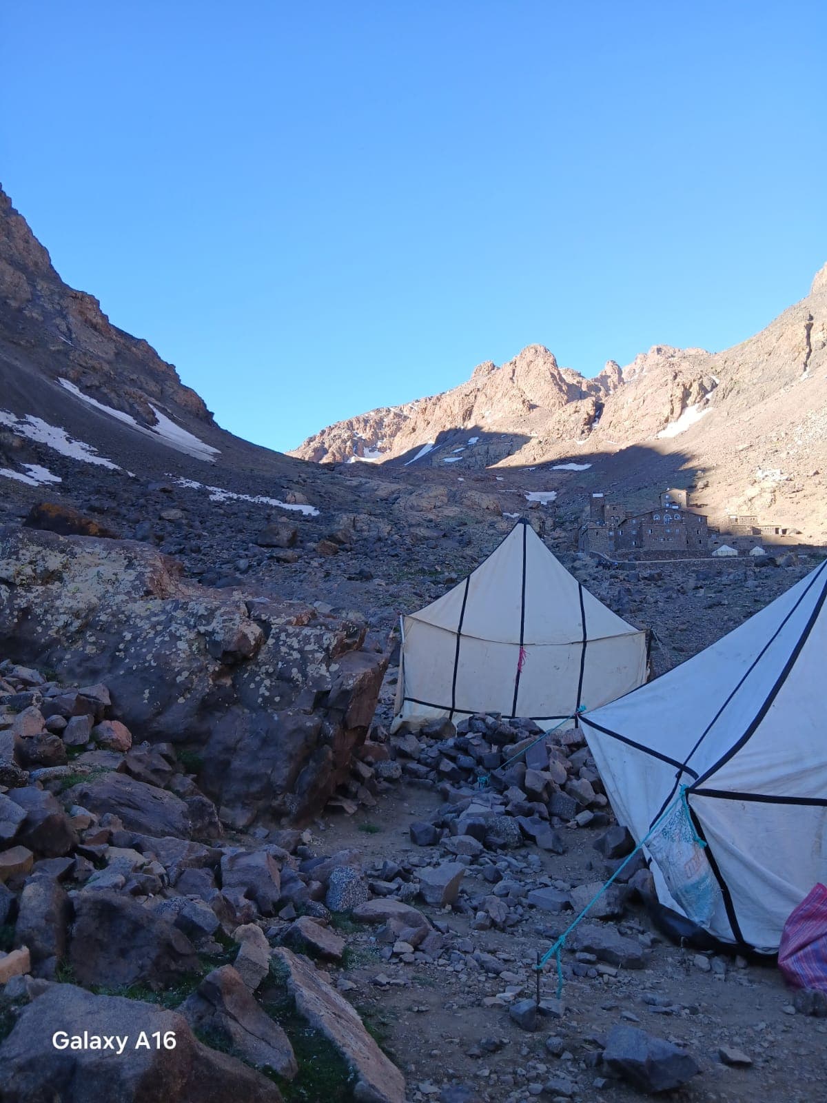 Two canvas trekking tents pitched on moraine below the Toubkal refuge at dawn, snow patches and the summit ridge behind