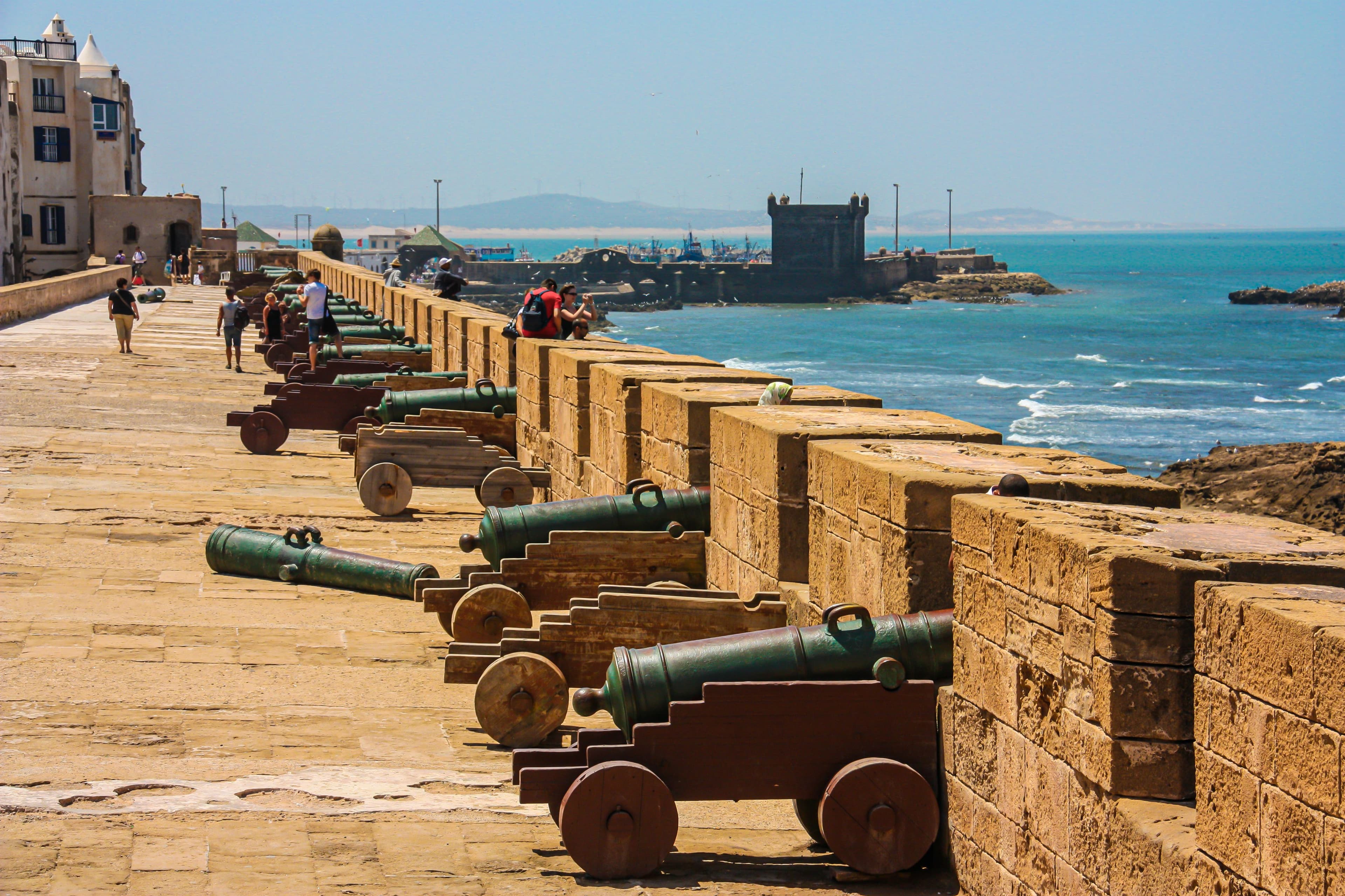 The Skala de la Ville ramparts at Essaouira, a row of bronze cannons on wooden carriages along the sea wall with the Atlantic and the harbour bastion beyond
