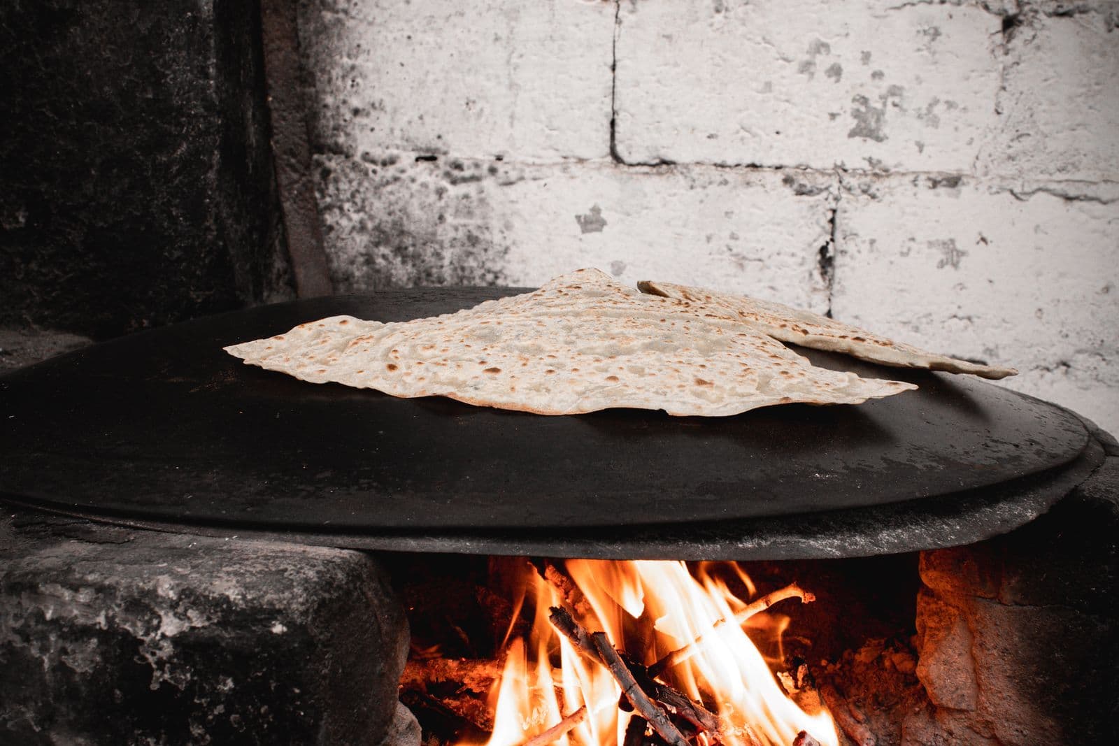 Thin flatbread cooking on a hot iron plate over an open wood fire in a stone hearth