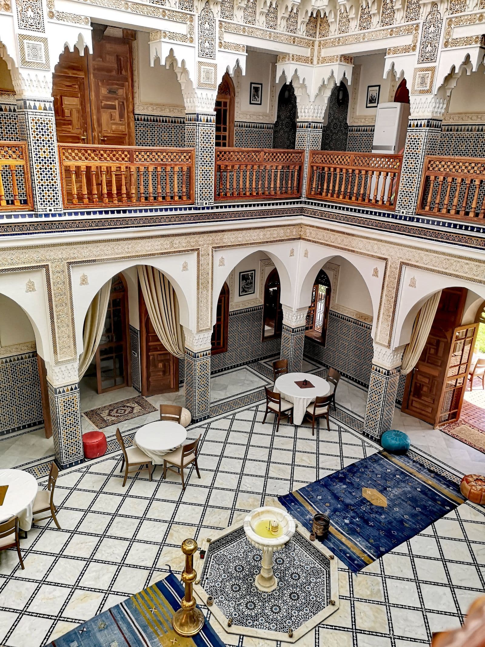 The tiled courtyard of a grand Moroccan riad, arcades and carved plaster on two storeys