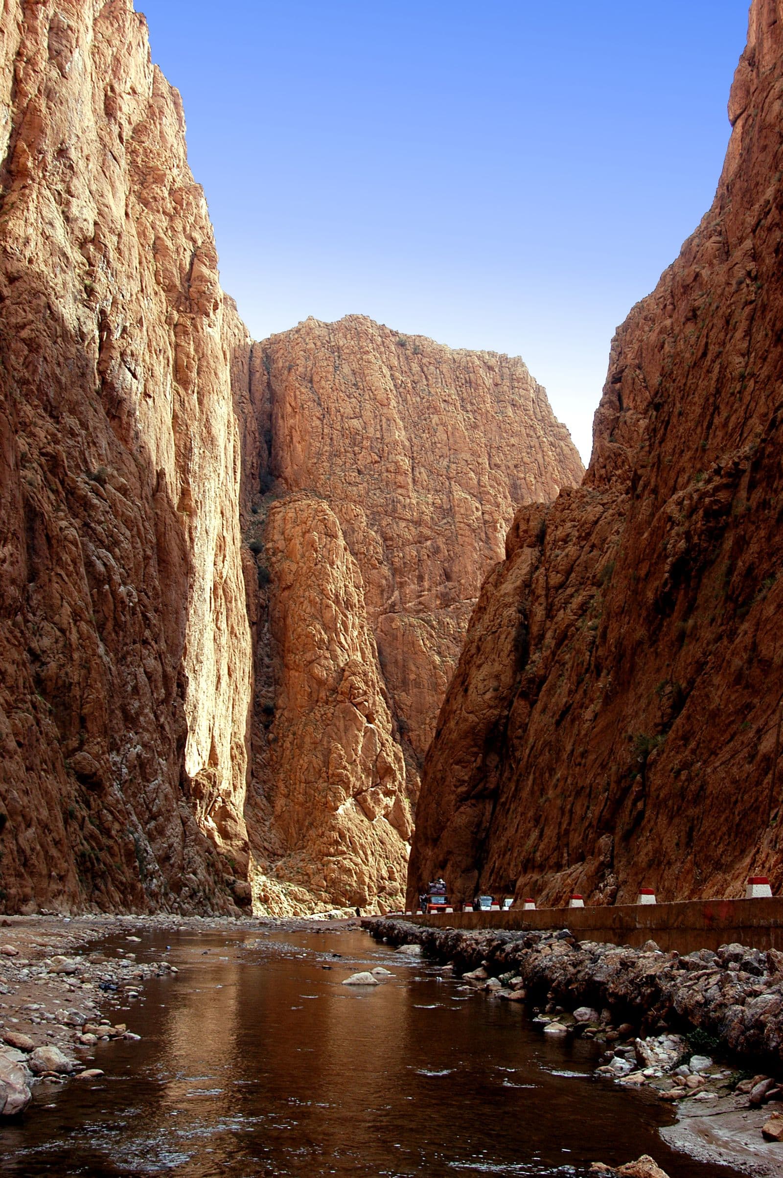 Sheer rock walls rising above a narrow gorge floor and a shallow stream