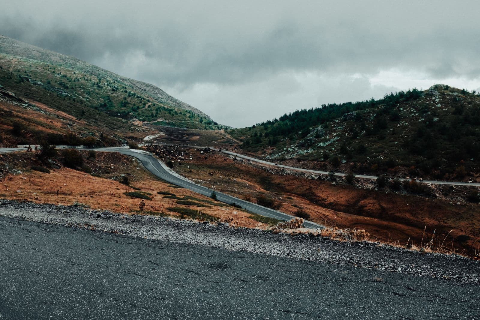 A winding mountain pass road cutting through bare upland slopes under heavy cloud